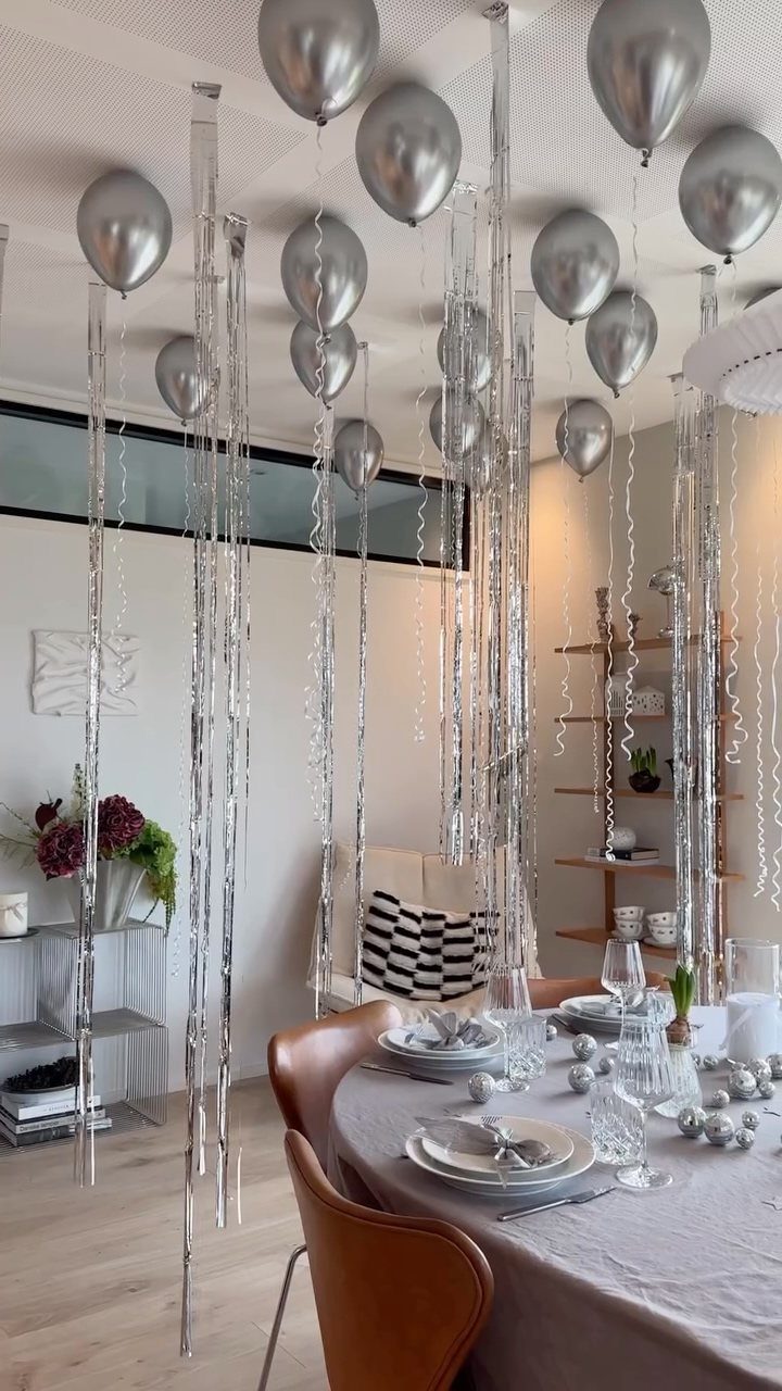 Dining table with grey linens and silver ornaments under floating silver balloons and streamers.