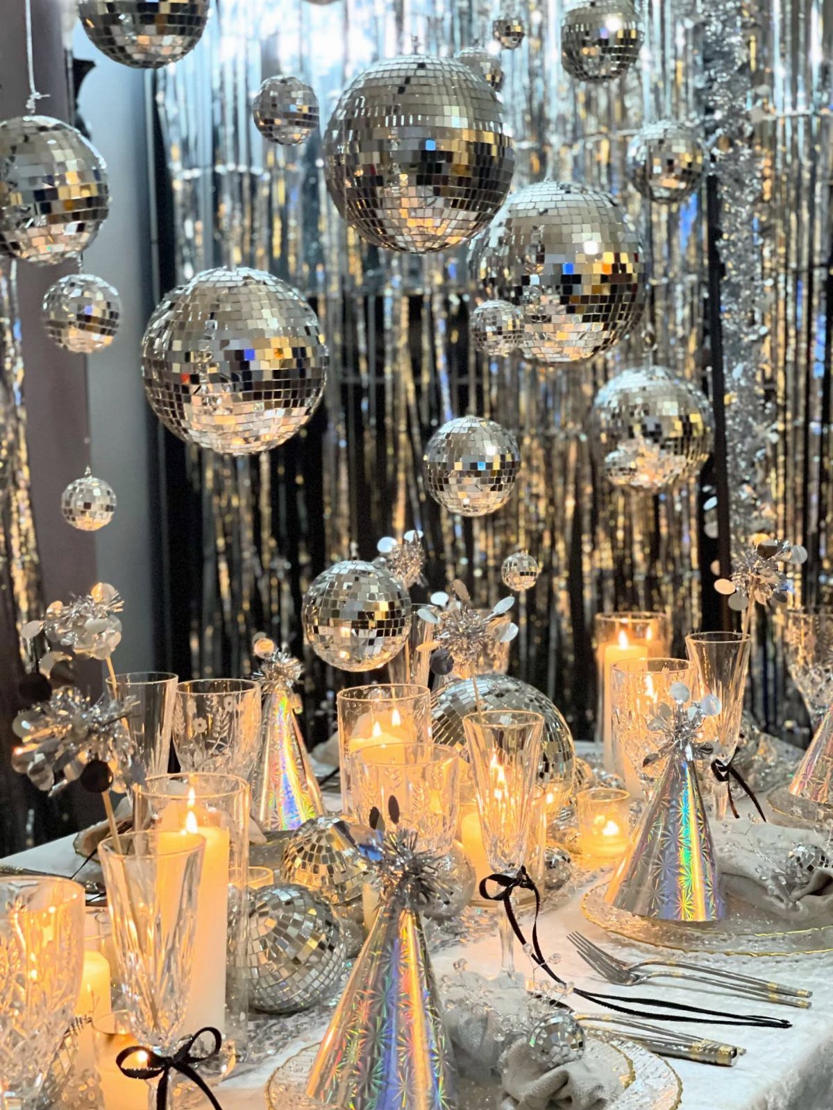 Silver holographic party hats on a festive table with candles and disco balls.