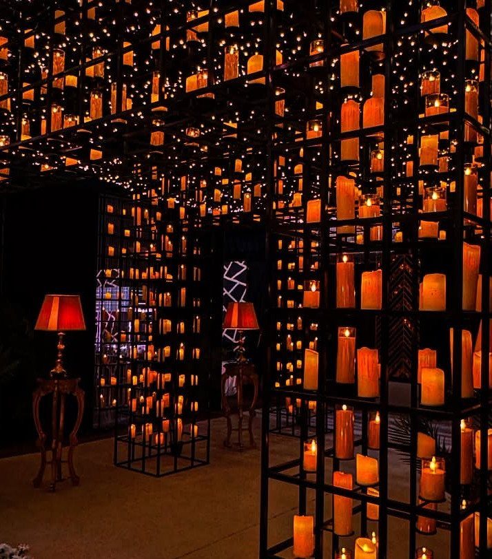 Glowing orange pillar candles and fairy lights arranged in black metal grid structures.