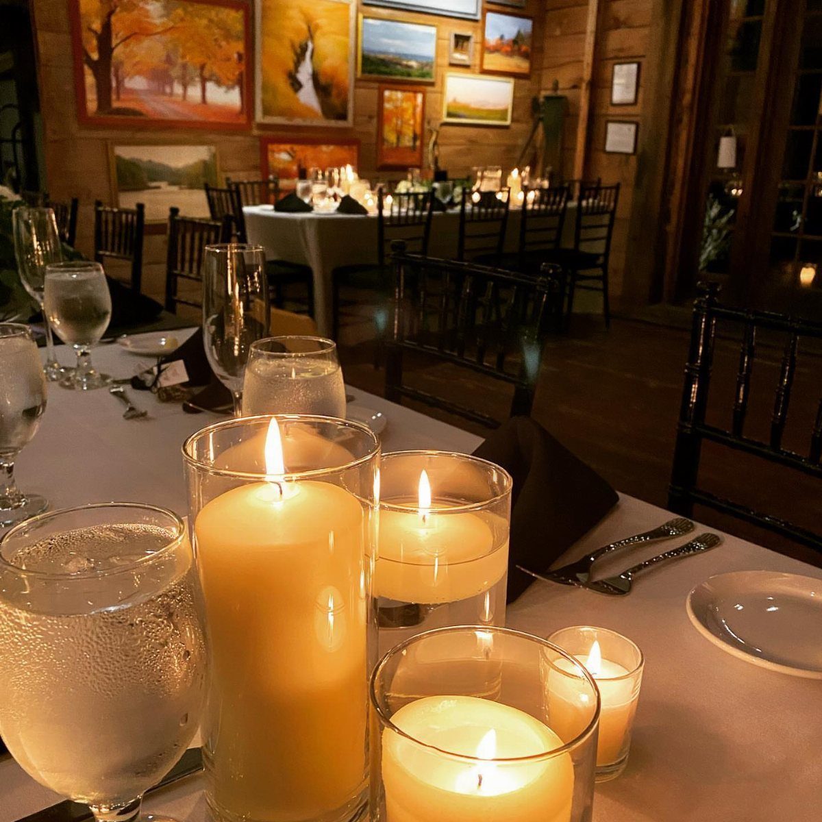 Lit cream candles in clear glass holders on a white wedding reception table.