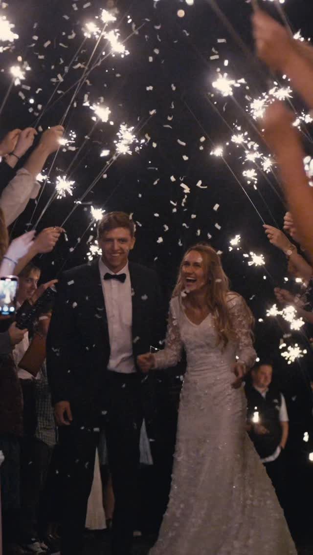 Bride and groom walking through a tunnel of glowing sparklers and falling confetti.