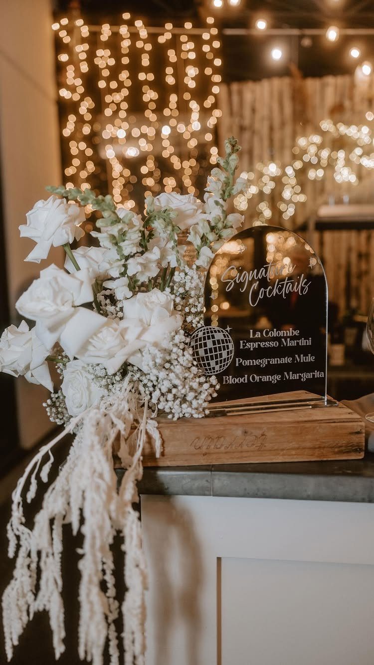 White floral arrangement and cocktail sign with a disco ball and fairy lights.