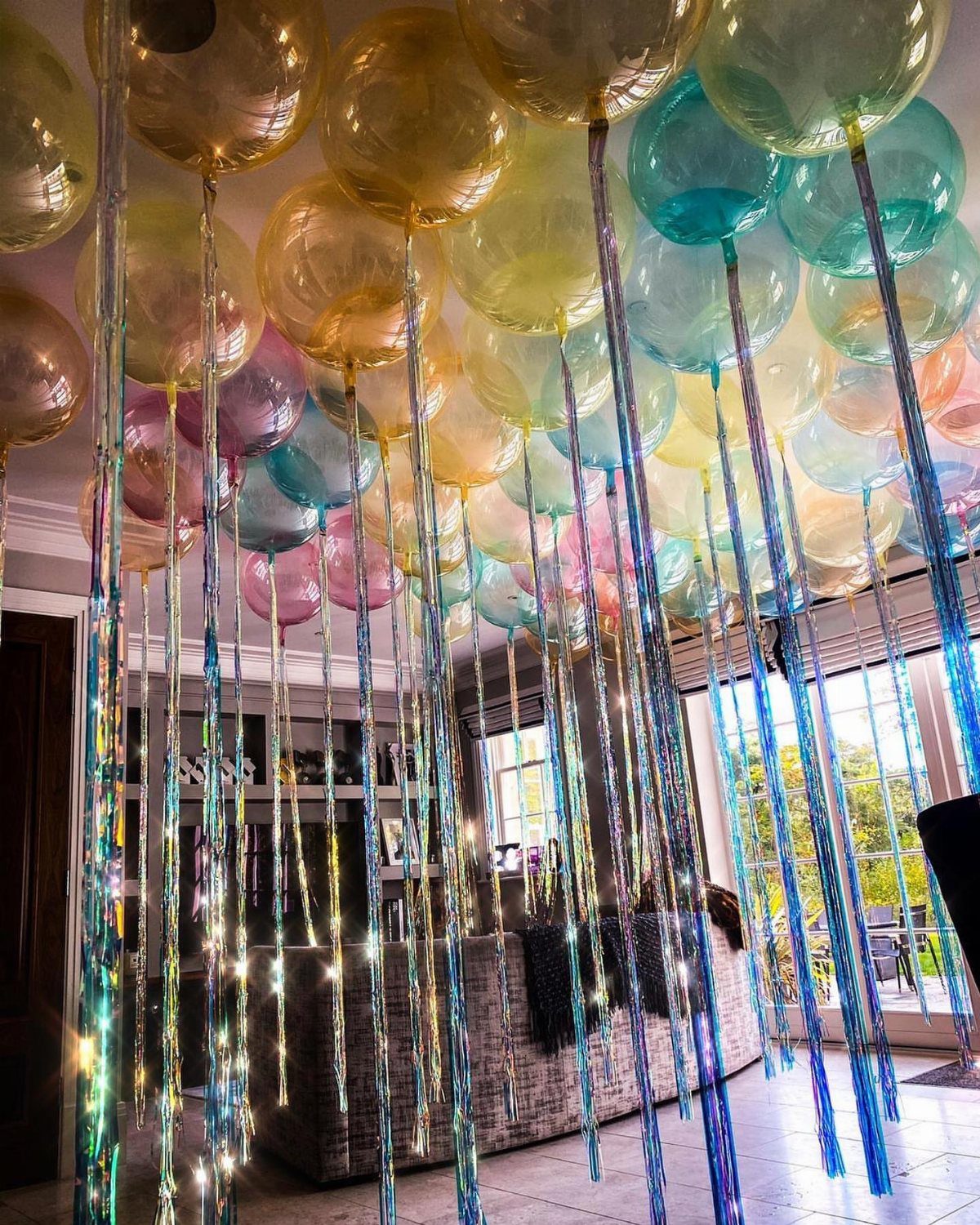 Colorful translucent balloons with shimmering metallic ribbons hanging from a white ceiling.