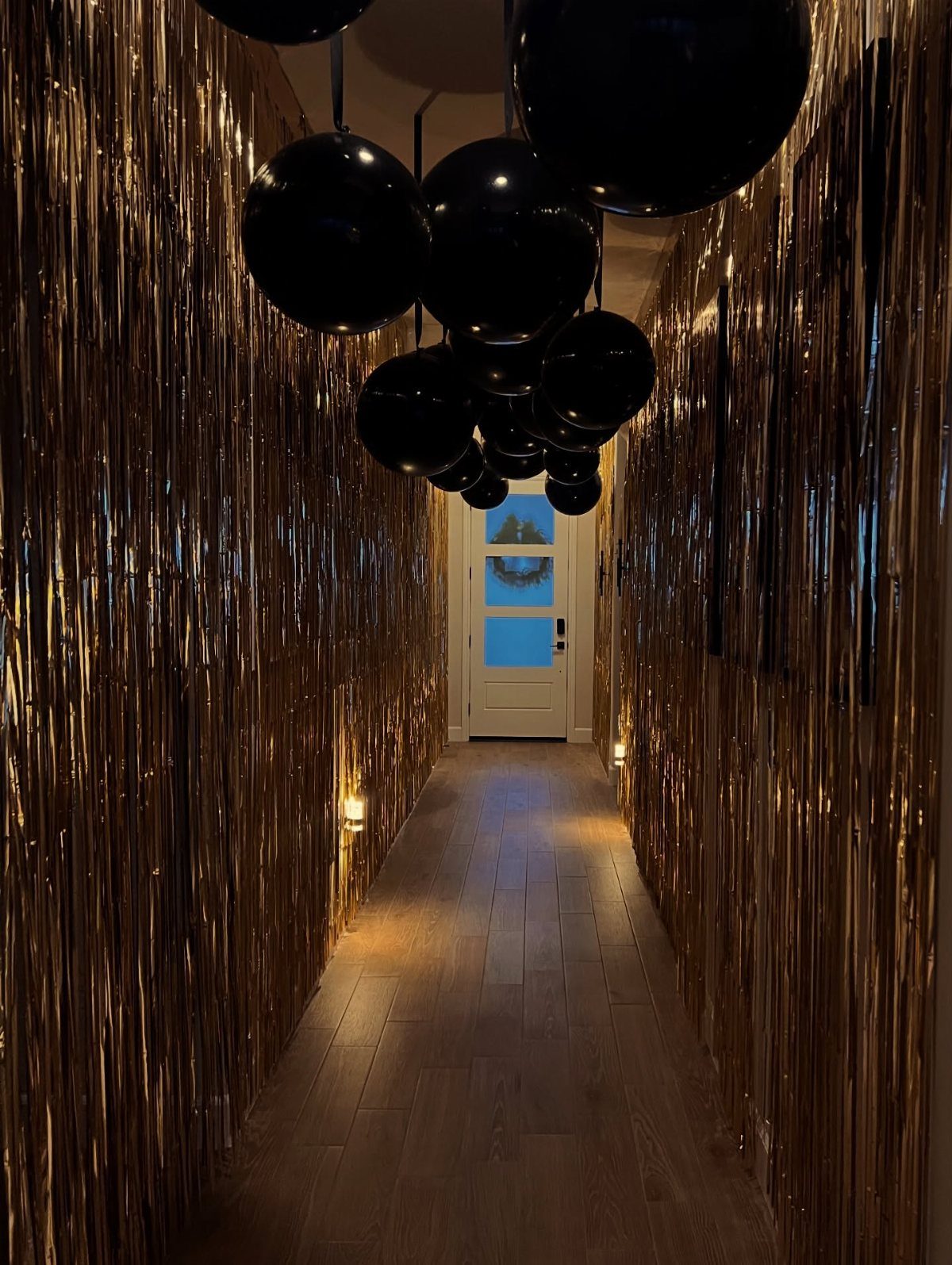 Gold foil fringe curtains and black balloons decorating a home hallway entryway.