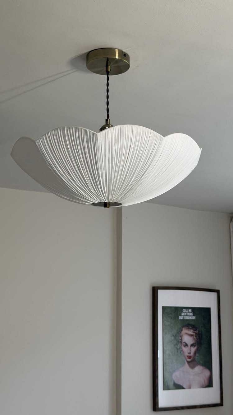 White pleated flower-shaped pendant light hanging in a room with a framed portrait.