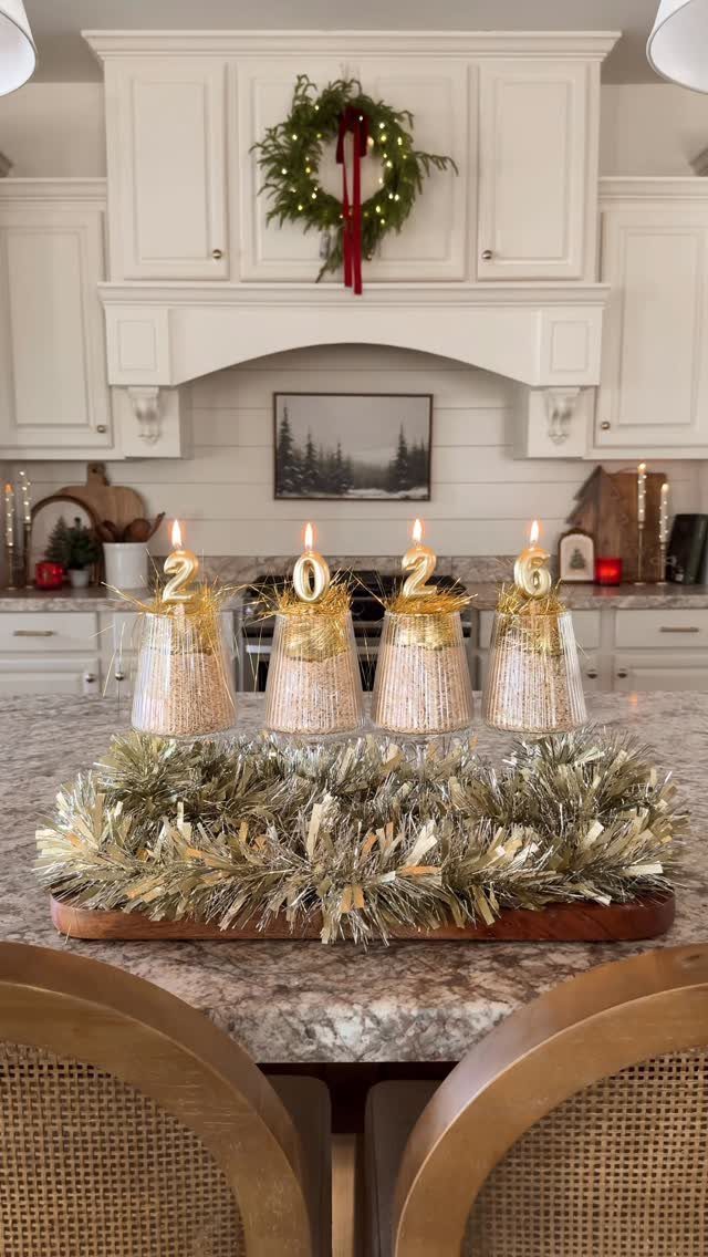 Glittery gold wine glasses with 2026 candles on a kitchen counter with tinsel.