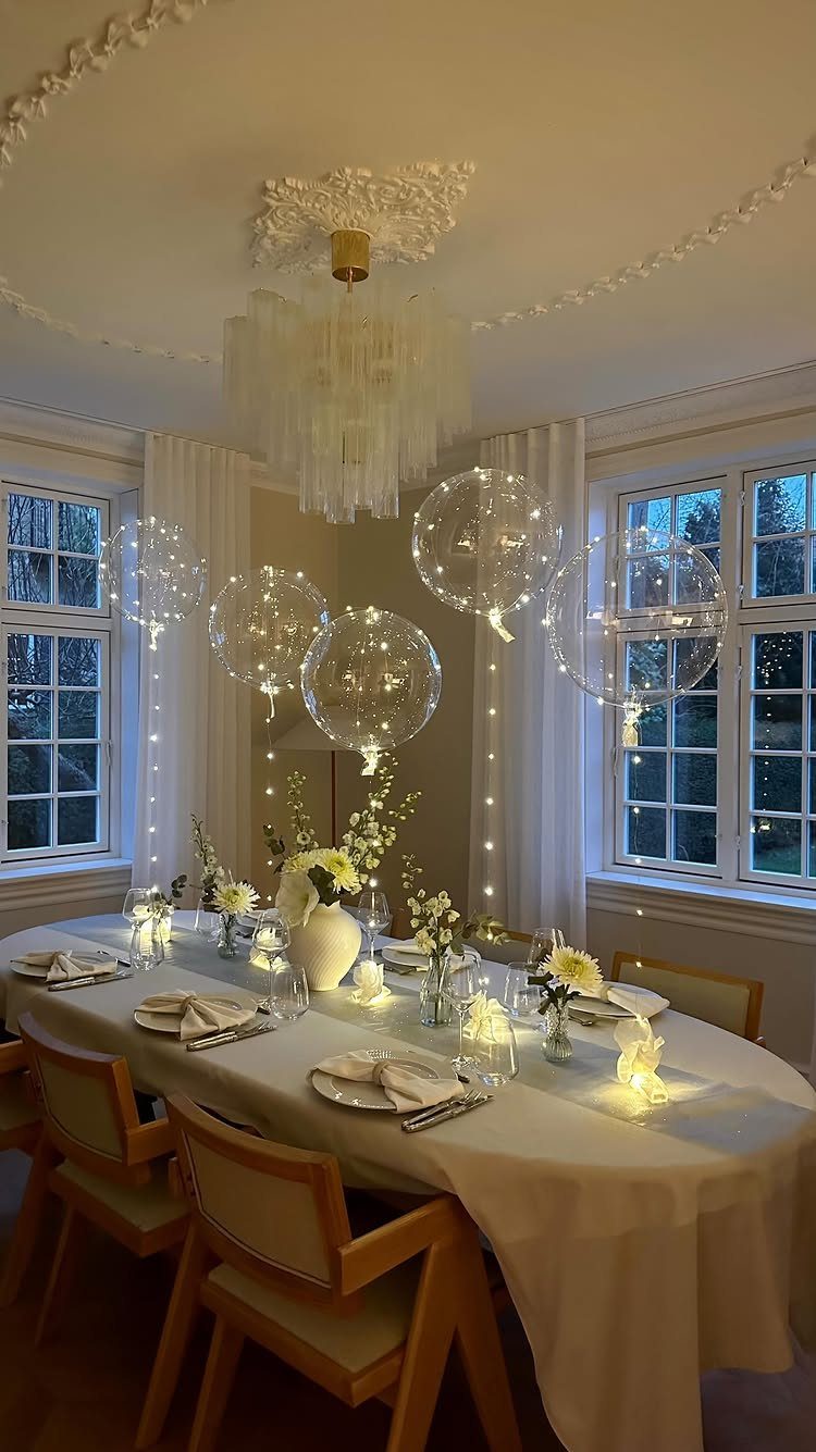 Dining table set with white linens, small white flowers, and floating light-filled balloons.