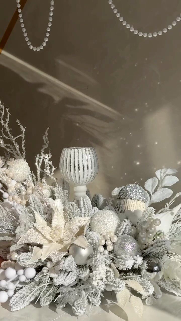 White and silver festive table arrangement with frosted foliage and glittery ornaments.