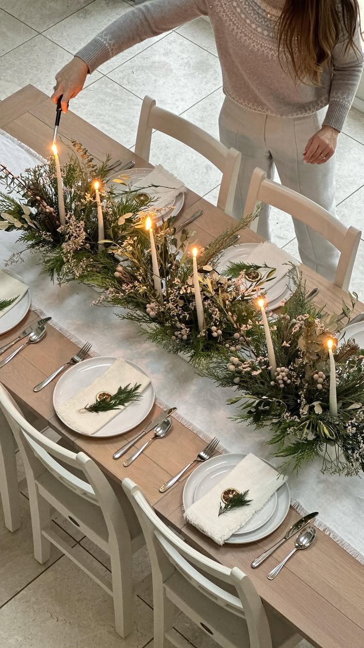Greenery garland table runner with white taper candles on a wooden dining table.