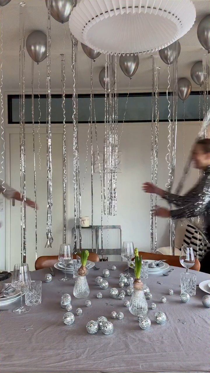 Festive table with silver ornaments, small plants, and hanging silver balloons and streamers.