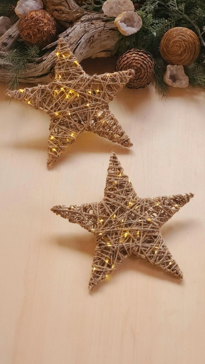 Two woven twine stars with warm fairy lights on a light wooden surface.