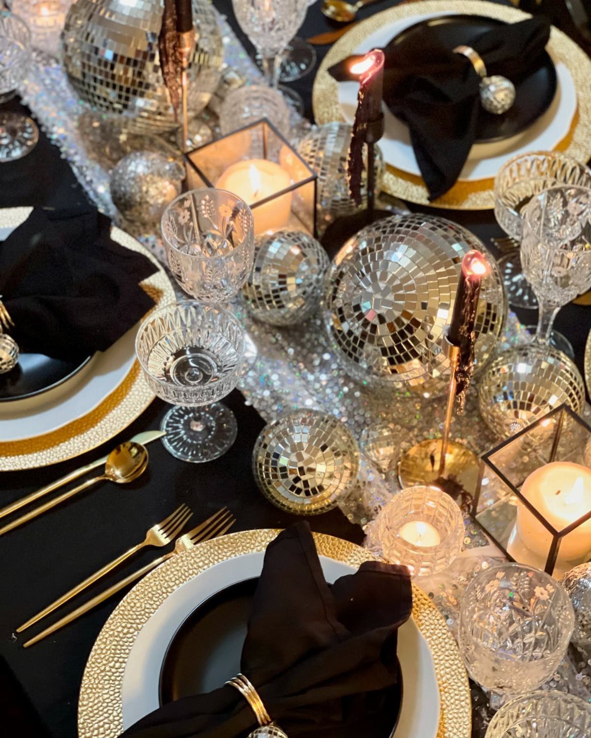 Festive table setting with a black tablecloth, silver sequin runner, and disco balls.