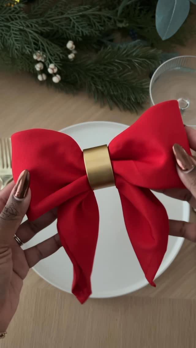 Red fabric napkin folded as a bow with a gold ring on a plate.