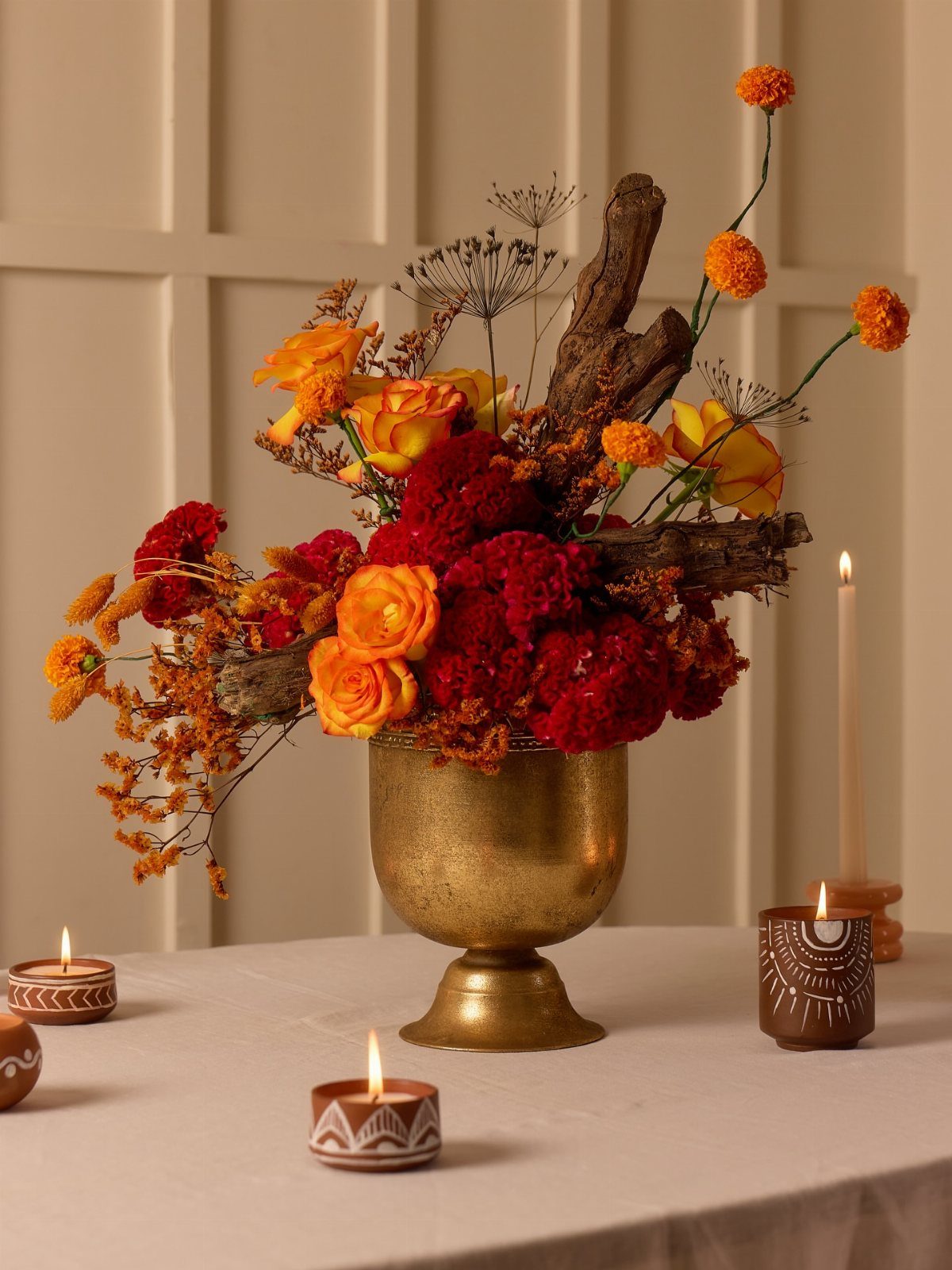 Floral arrangement in a gold vase with lit candles on a white table