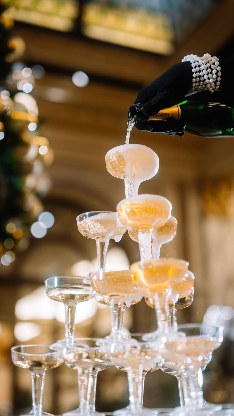 Champagne pouring into a tower of coupe glasses with a gloved hand.