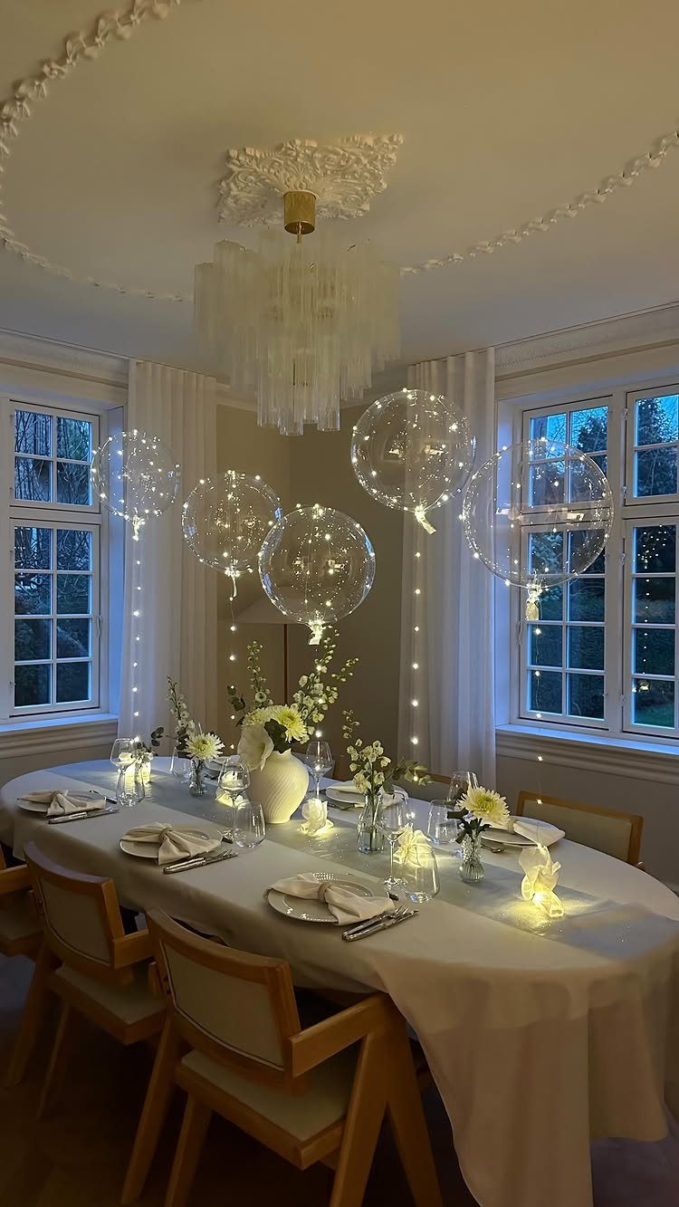 Dining table with white linens, floral centerpieces, and floating light-filled balloons above.