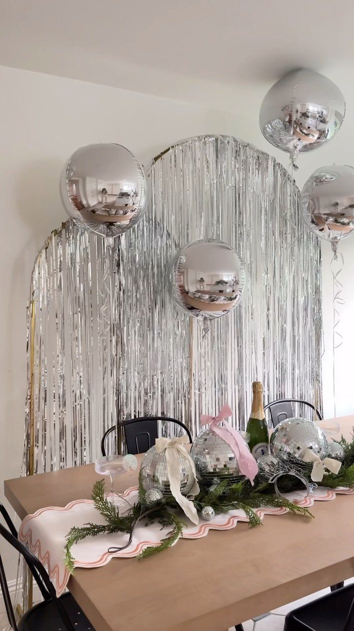 Wooden table with silver ornaments and champagne against a silver tinsel backdrop.