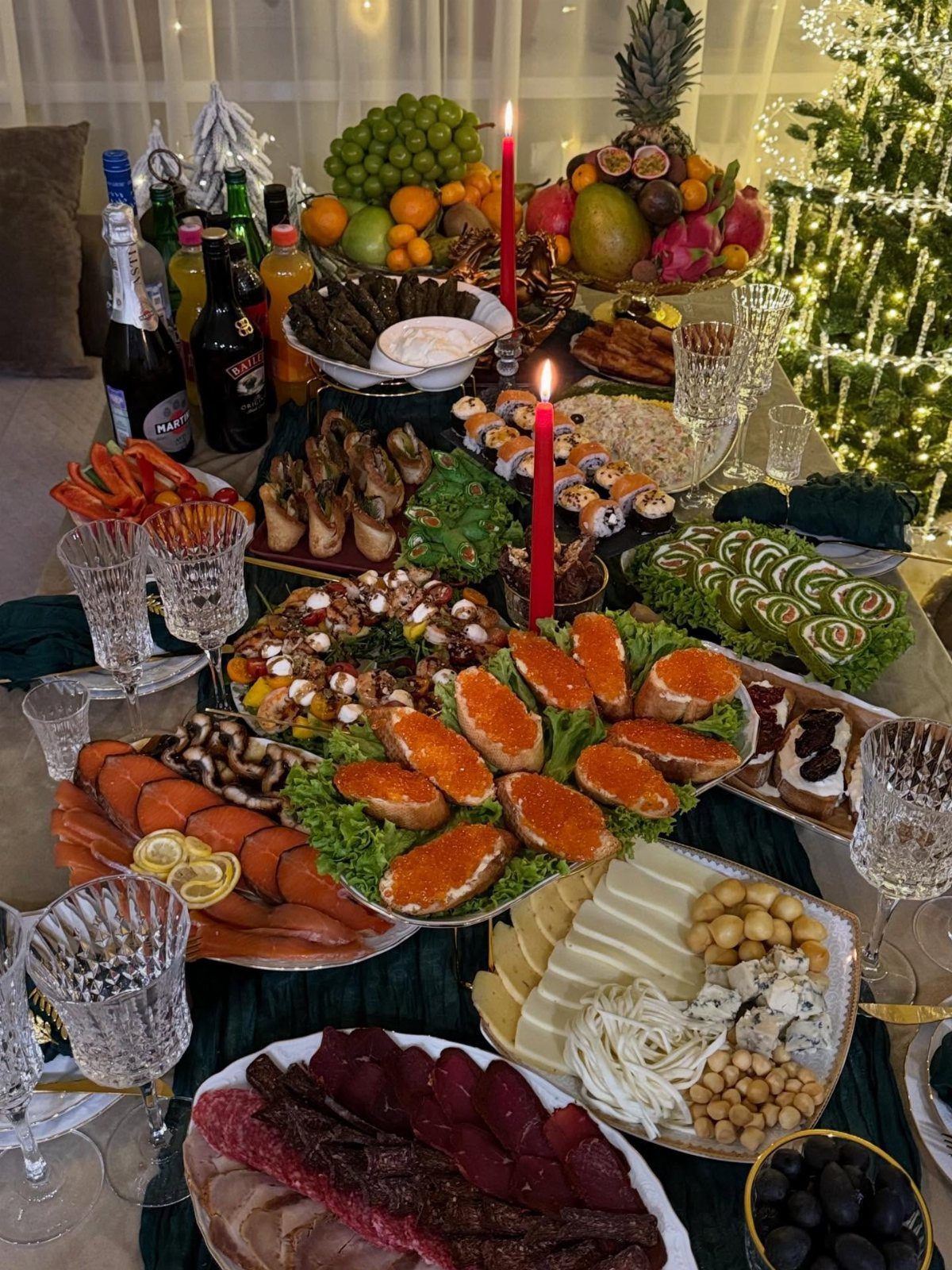 Festive table spread with caviar, salmon, cheeses, and fruit with red candles.