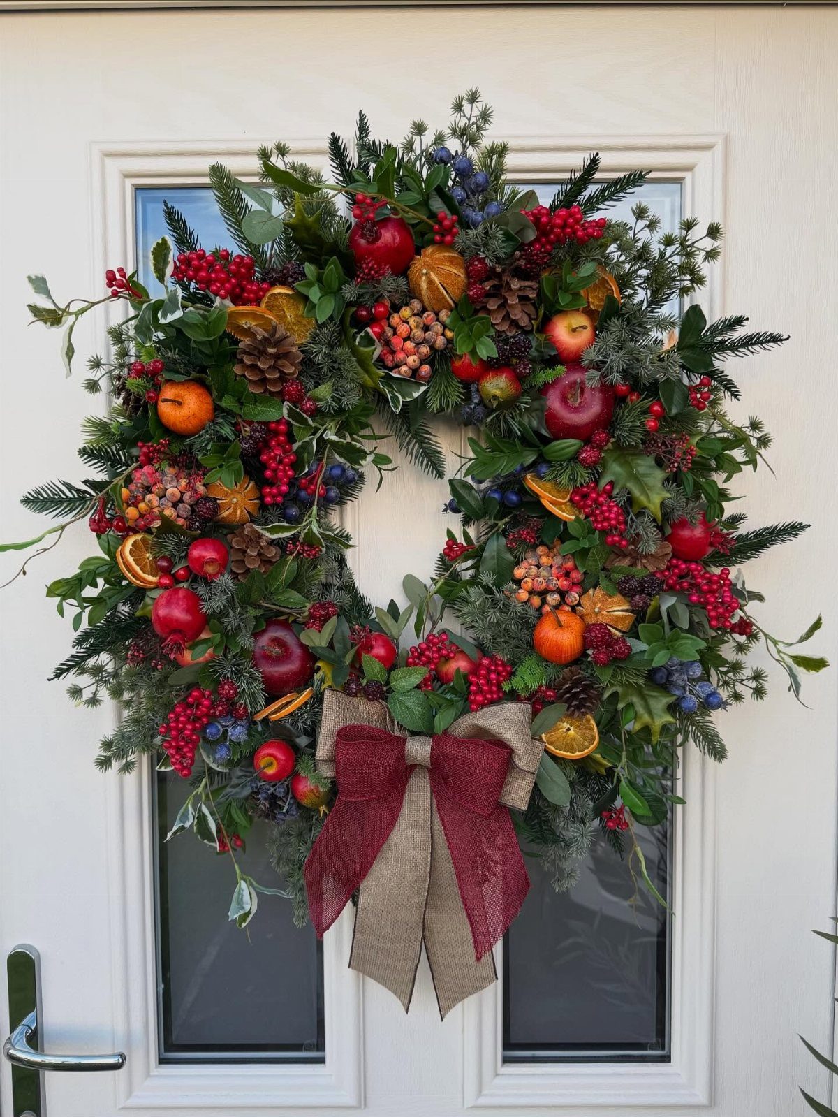 Holiday wreath with evergreen branches, red apples, orange slices, and a burlap bow.