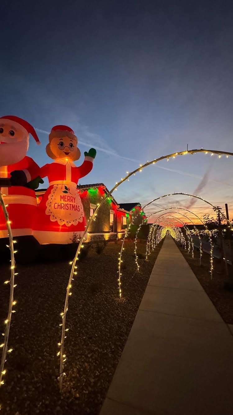 Glowing light arches forming a tunnel over a walkway with inflatable Christmas figures.