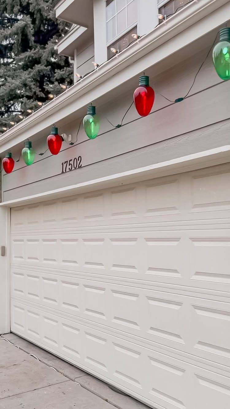 Giant red and green Christmas light decorations hanging above a white garage door.