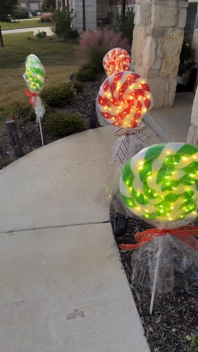 Giant red and green swirl lollipop decorations with lights along a garden path