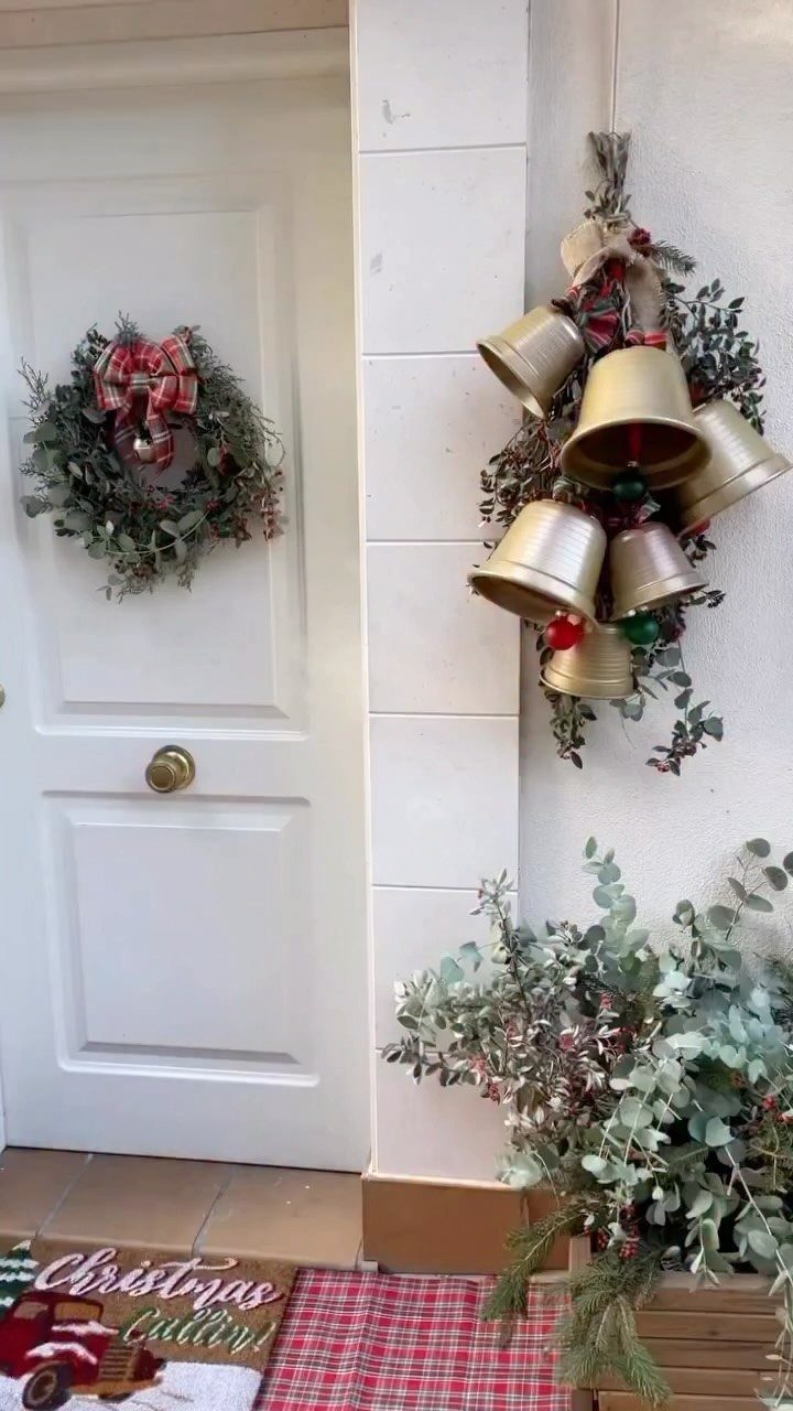 Gold Christmas bells with greenery hanging on a white wall next to a door.