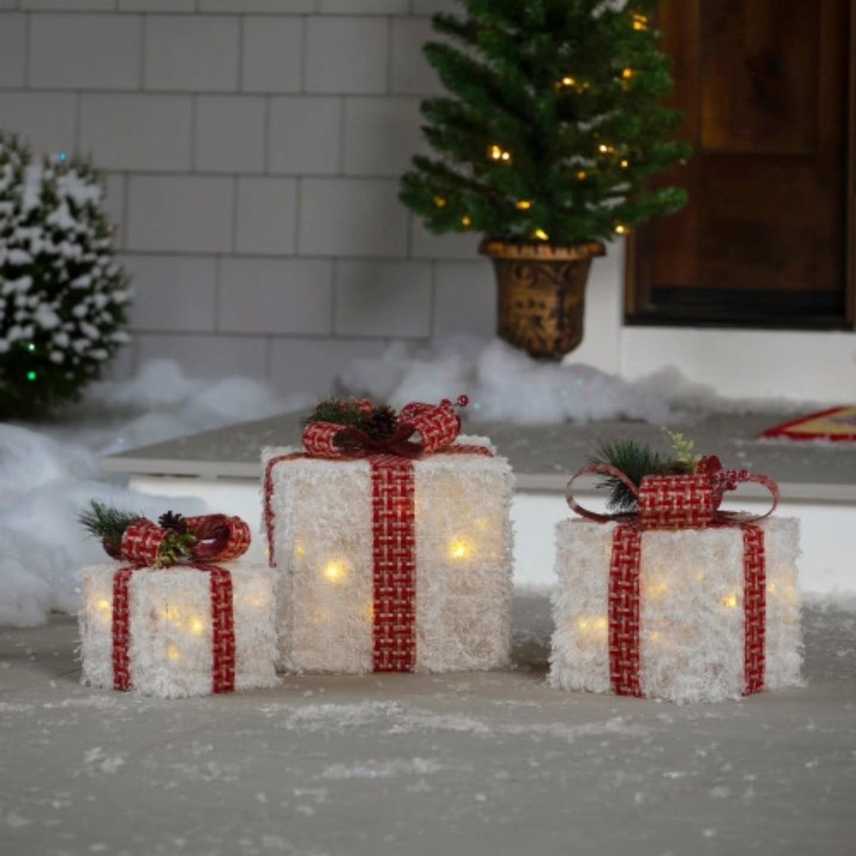 Three white illuminated gift boxes with red checkered ribbons on a snowy surface.