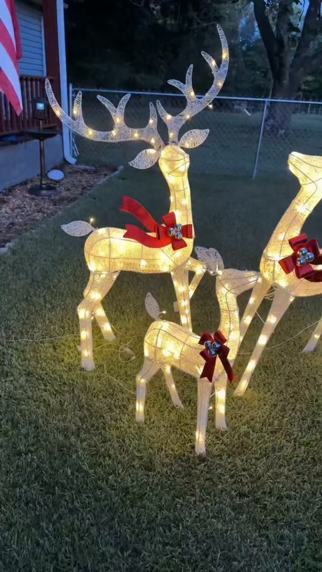 Three glowing reindeer figures with red bows standing on a green grass lawn.