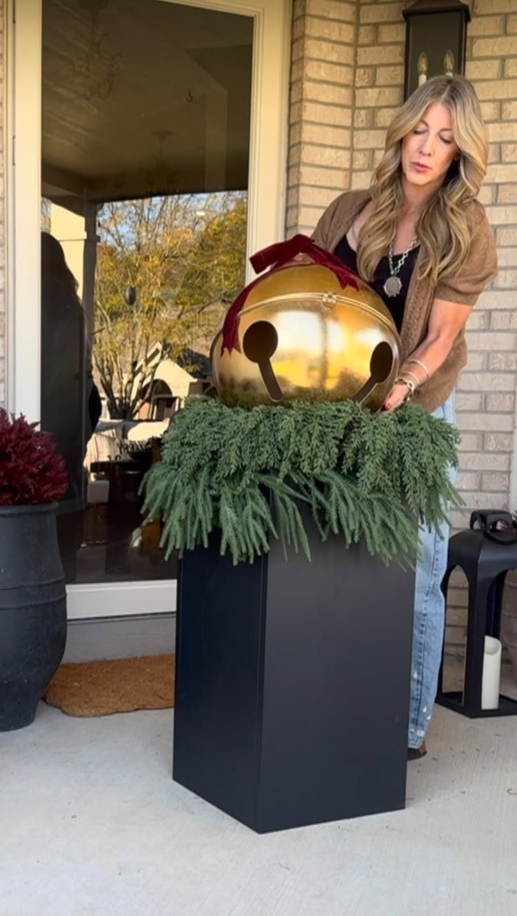 Large gold acorn ornament on green garland atop a black pedestal on a porch