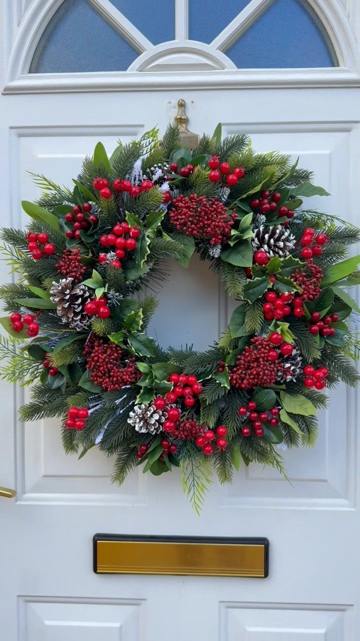 Christmas wreath with pinecones and red berries hanging on a white front door