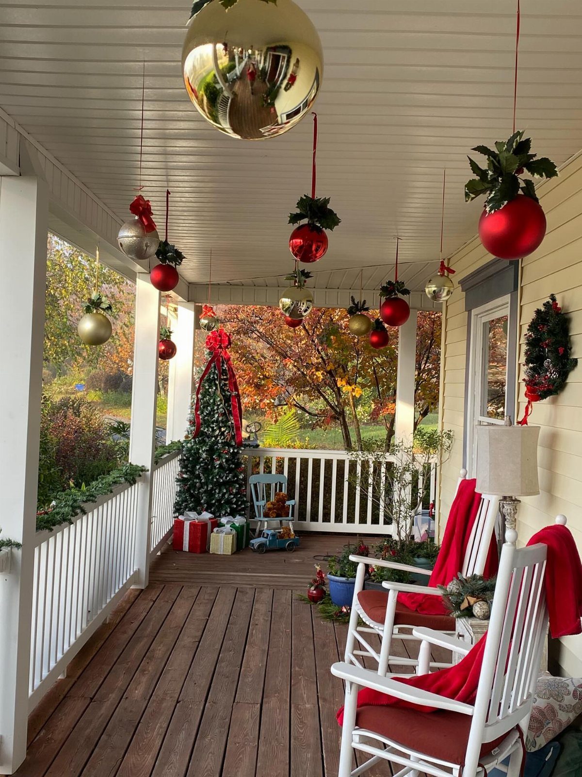 Decorated porch with a lit Christmas tree, hanging ornaments, and a white rocking chair.