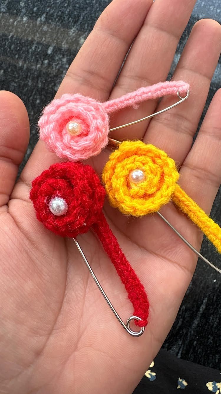 Three colorful crochet flower pins with pearl centers held in a person's palm.