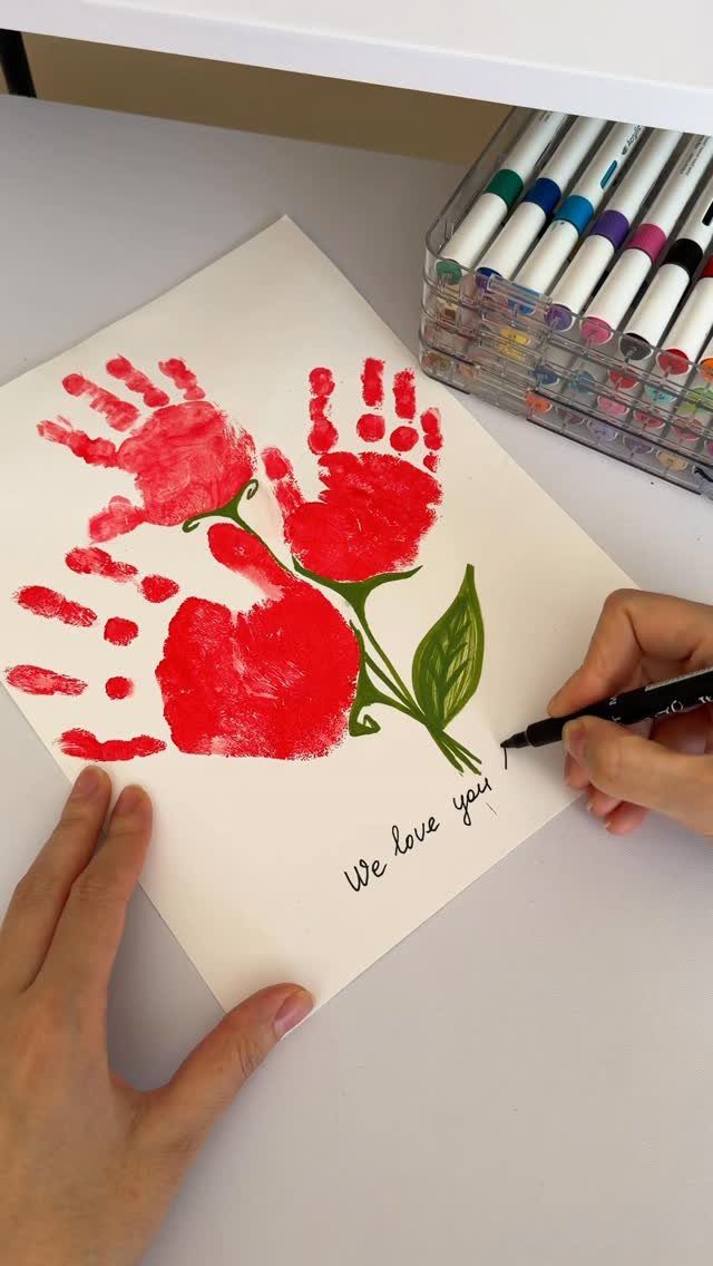 Red handprint flowers on white paper with a person writing We love you