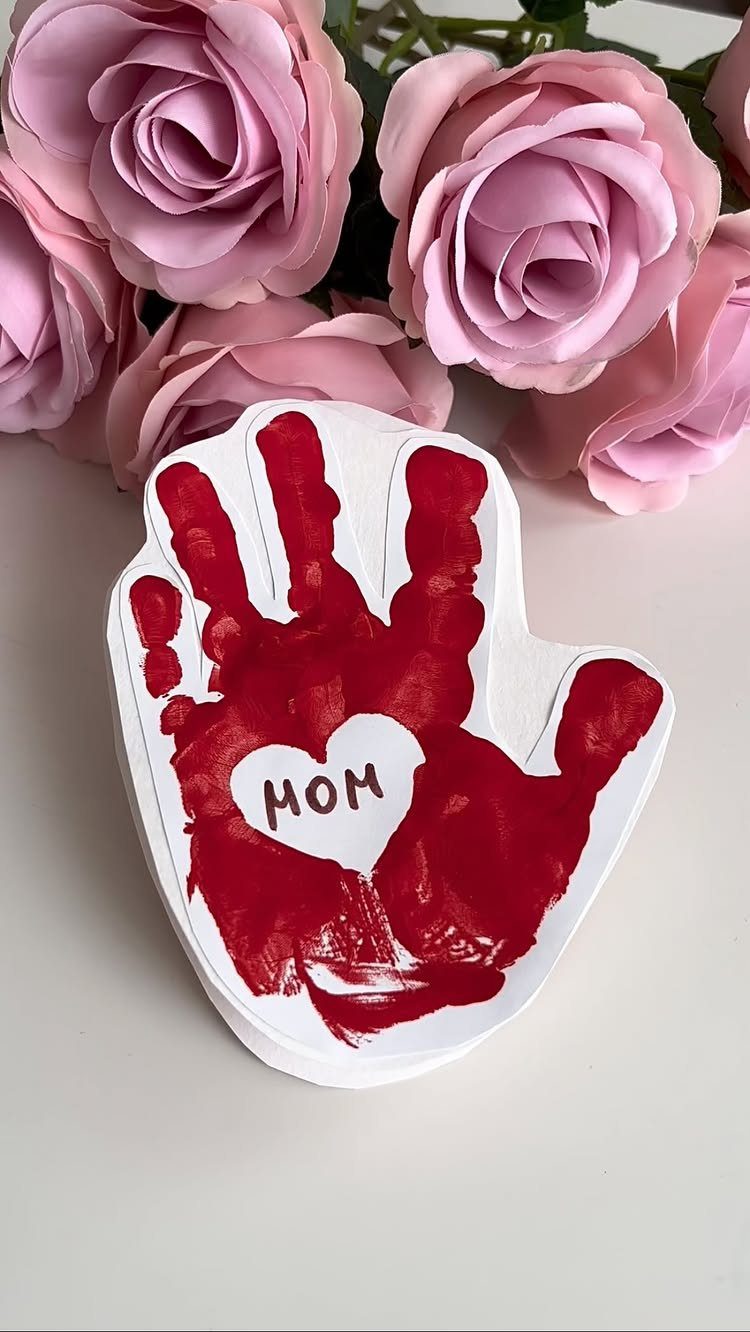 Red handprint craft on a white hand-shaped card with a heart saying MOM.