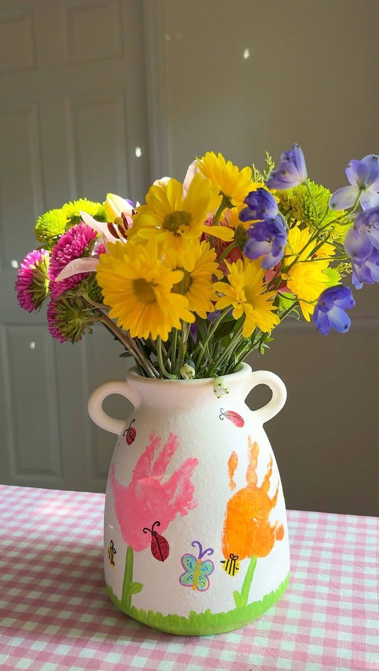 White ceramic vase with colorful handprints holding a bouquet of bright spring flowers.