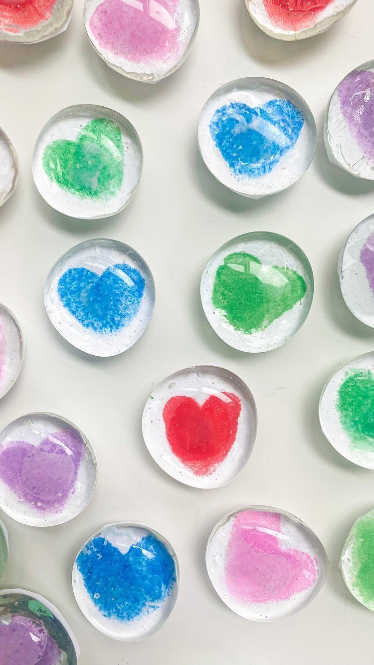 Colorful painted hearts on small round glass stones scattered on a white background