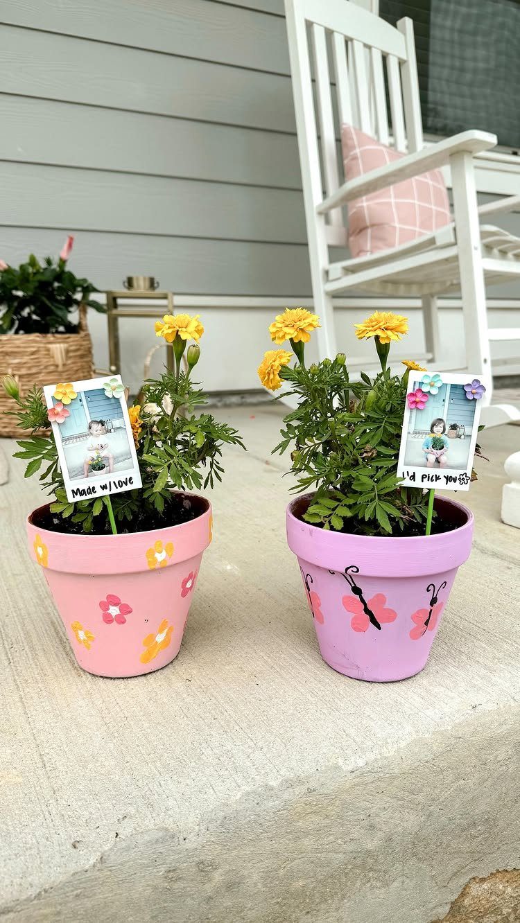 Two painted pink and purple flower pots with yellow marigolds and child photos.