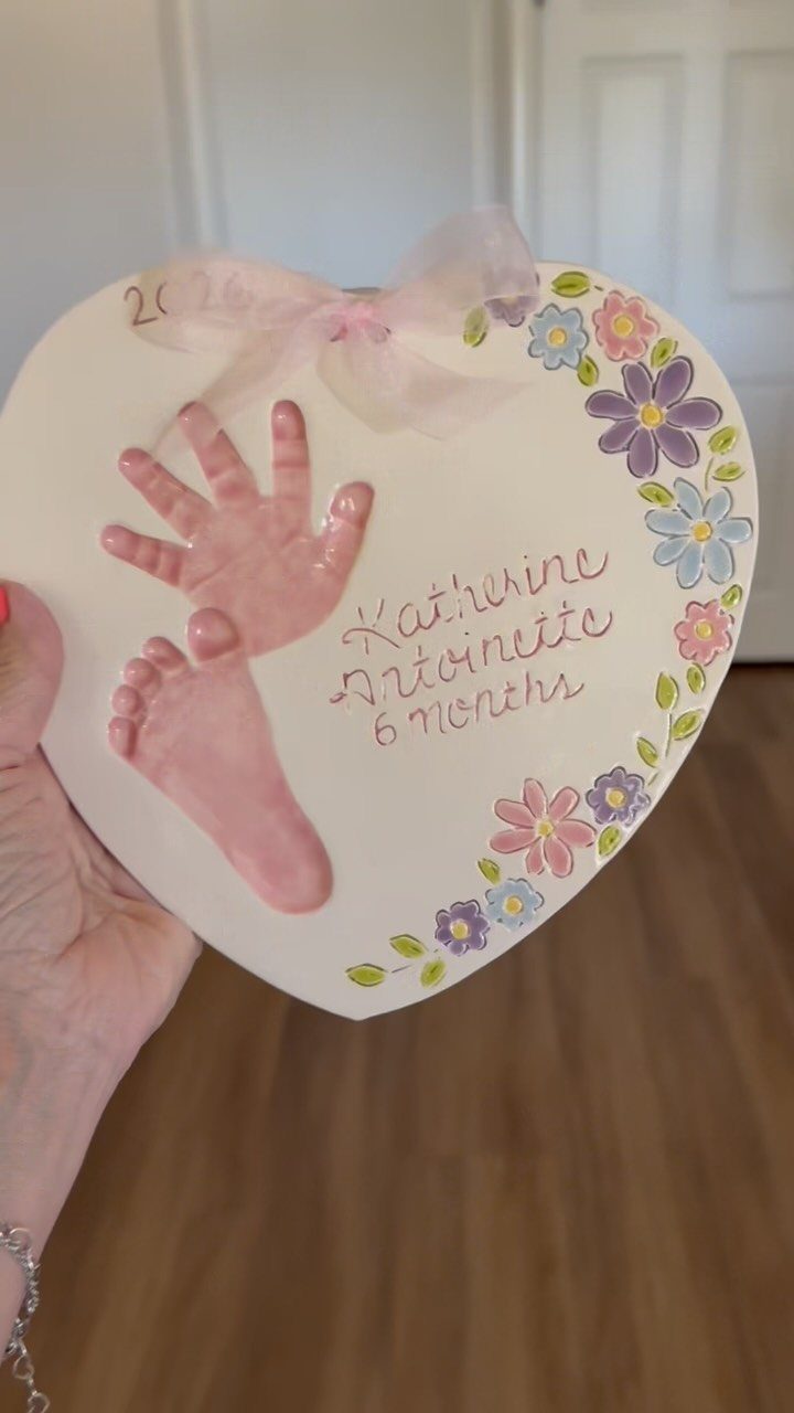 Heart-shaped salt dough plaque with pink baby handprint, footprint, and painted flowers.