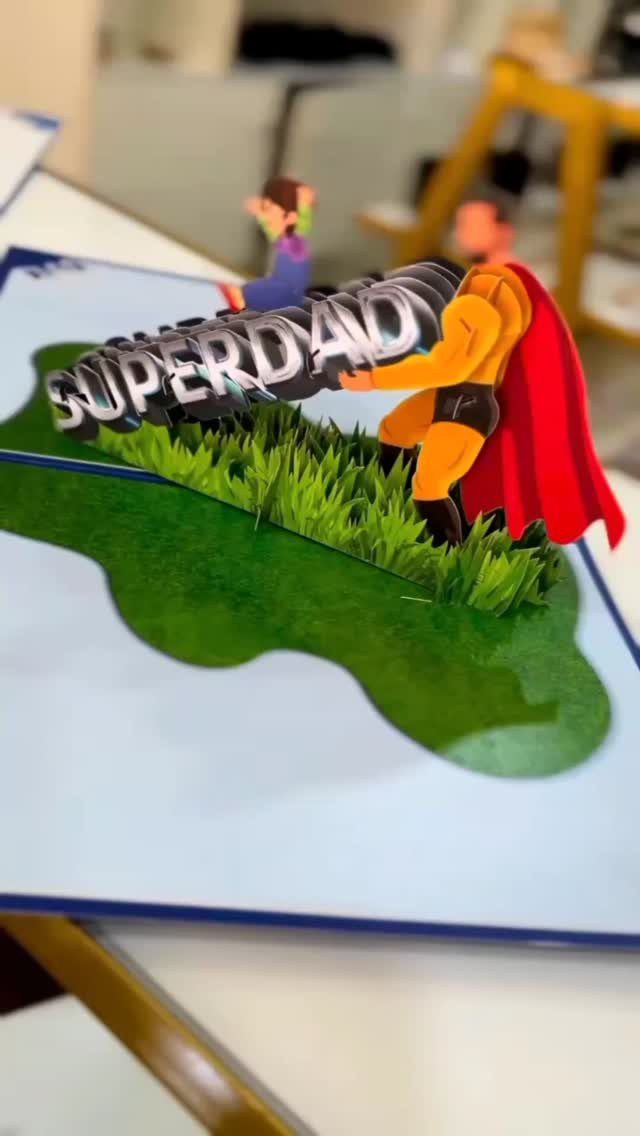 3D pop-up card with a superhero pushing silver SUPER DAD letters on grass