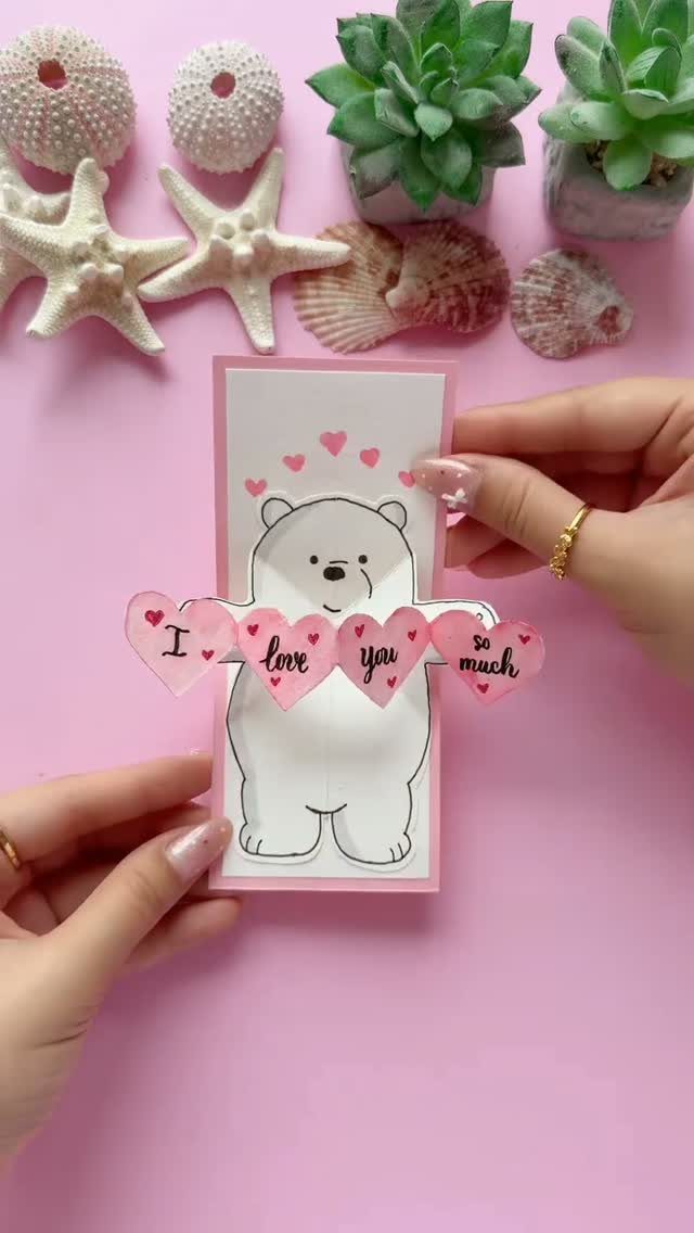 Polar bear Valentine card with pink hearts held by two hands on pink background