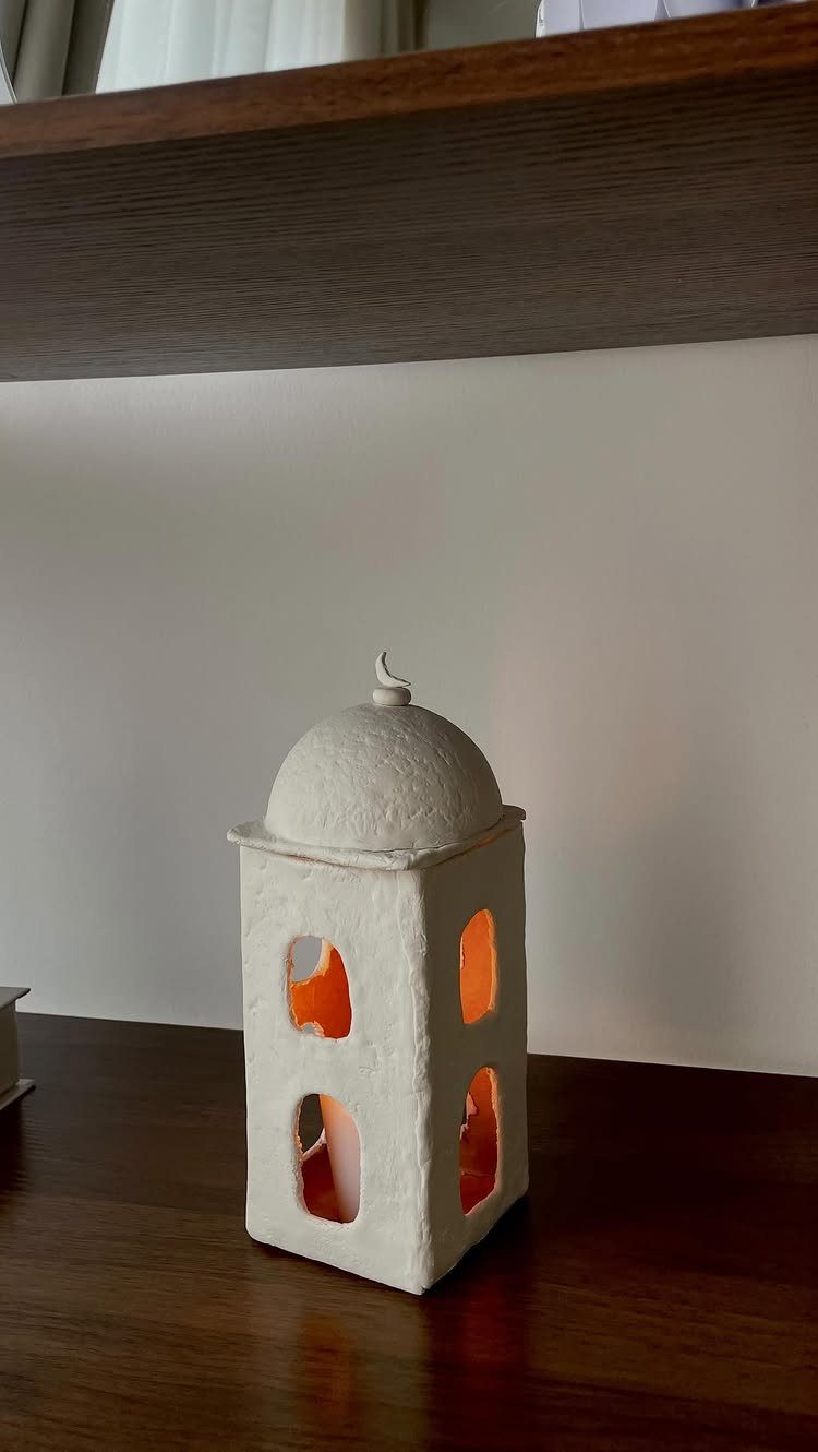 White ceramic candle lantern with a domed top glowing on a wooden shelf.