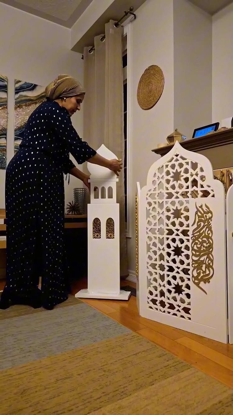 Woman adjusting a white minaret decoration next to a carved Islamic screen.