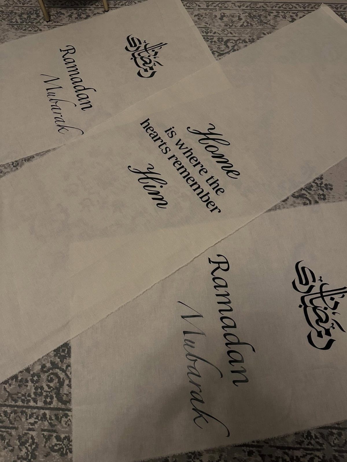 White paper banners with Ramadan Mubarak and religious quotes on a patterned carpet.
