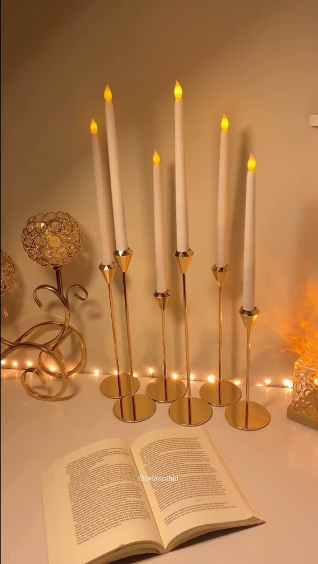 White electric taper candles in gold holders next to an open book.