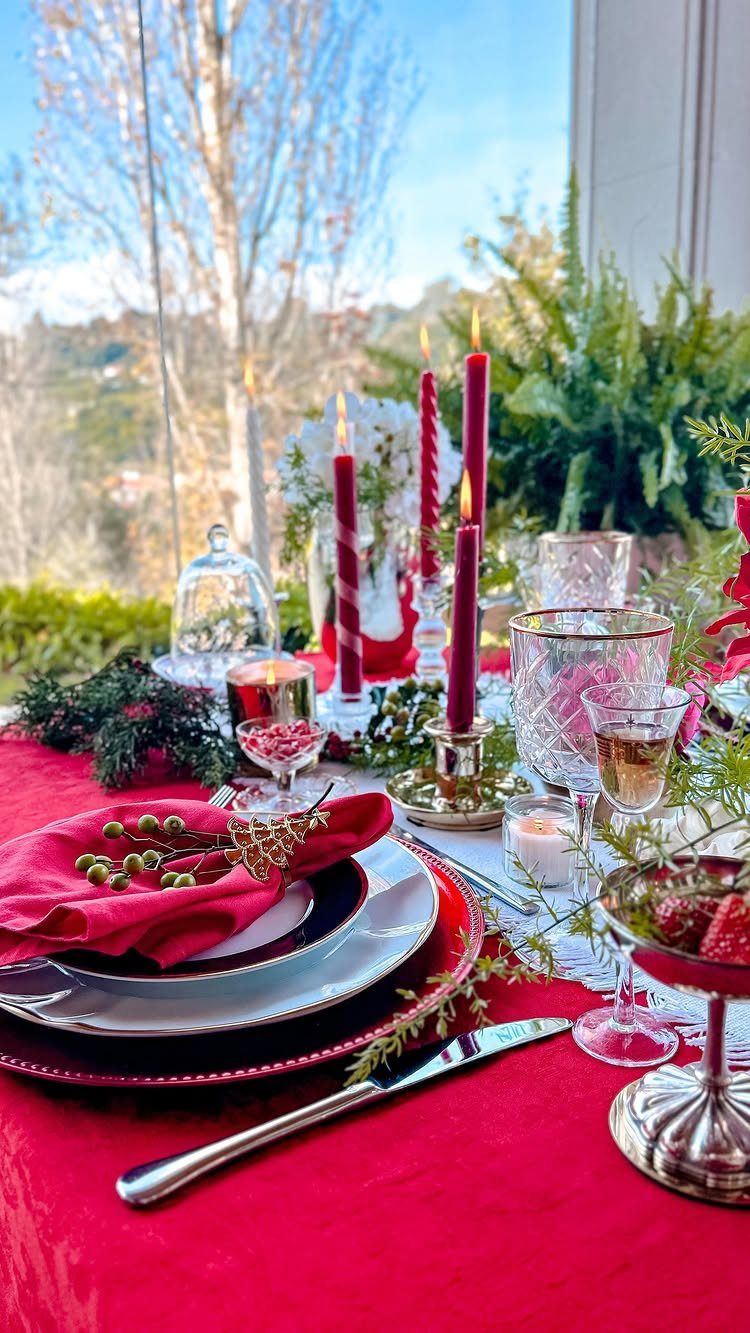 Festive dining table set with red linens, red candles, and holiday greenery.