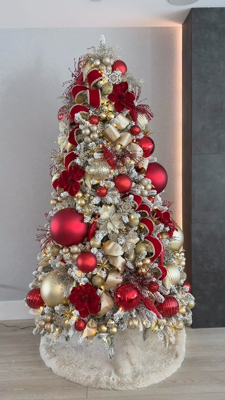 White flocked Christmas tree decorated with red and gold ornaments and red flowers.