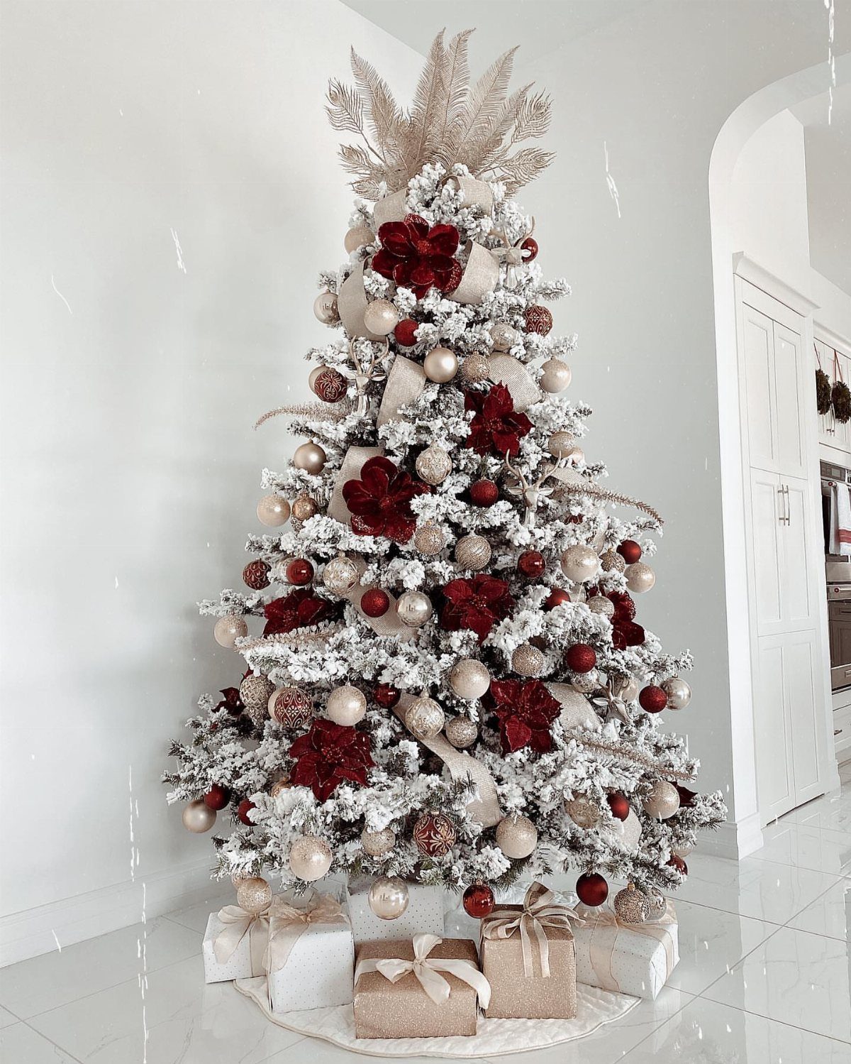 Flocked Christmas tree decorated with red and gold ornaments and red floral accents.