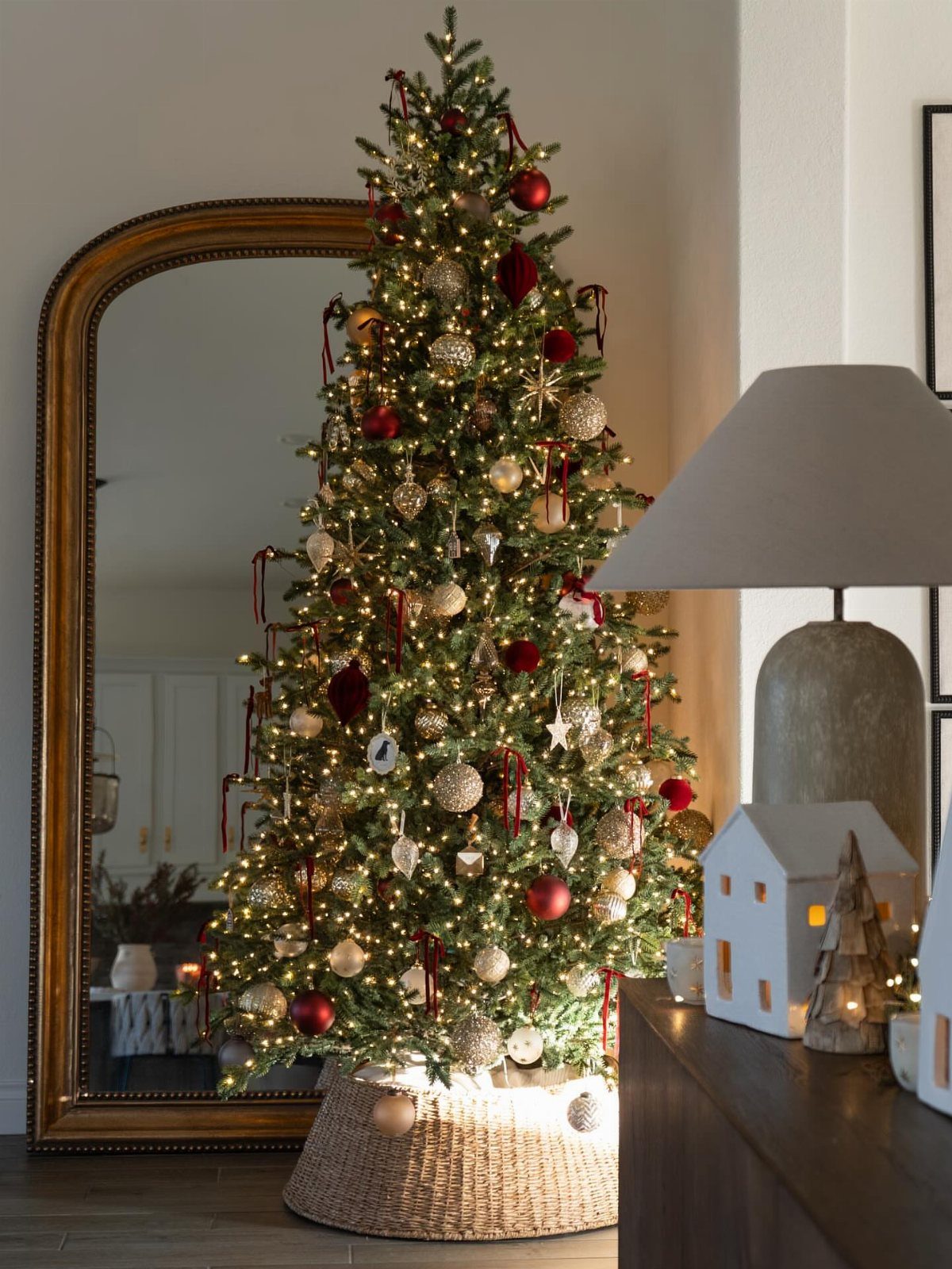 Decorated Christmas tree with red and gold ornaments standing beside a gold mirror.