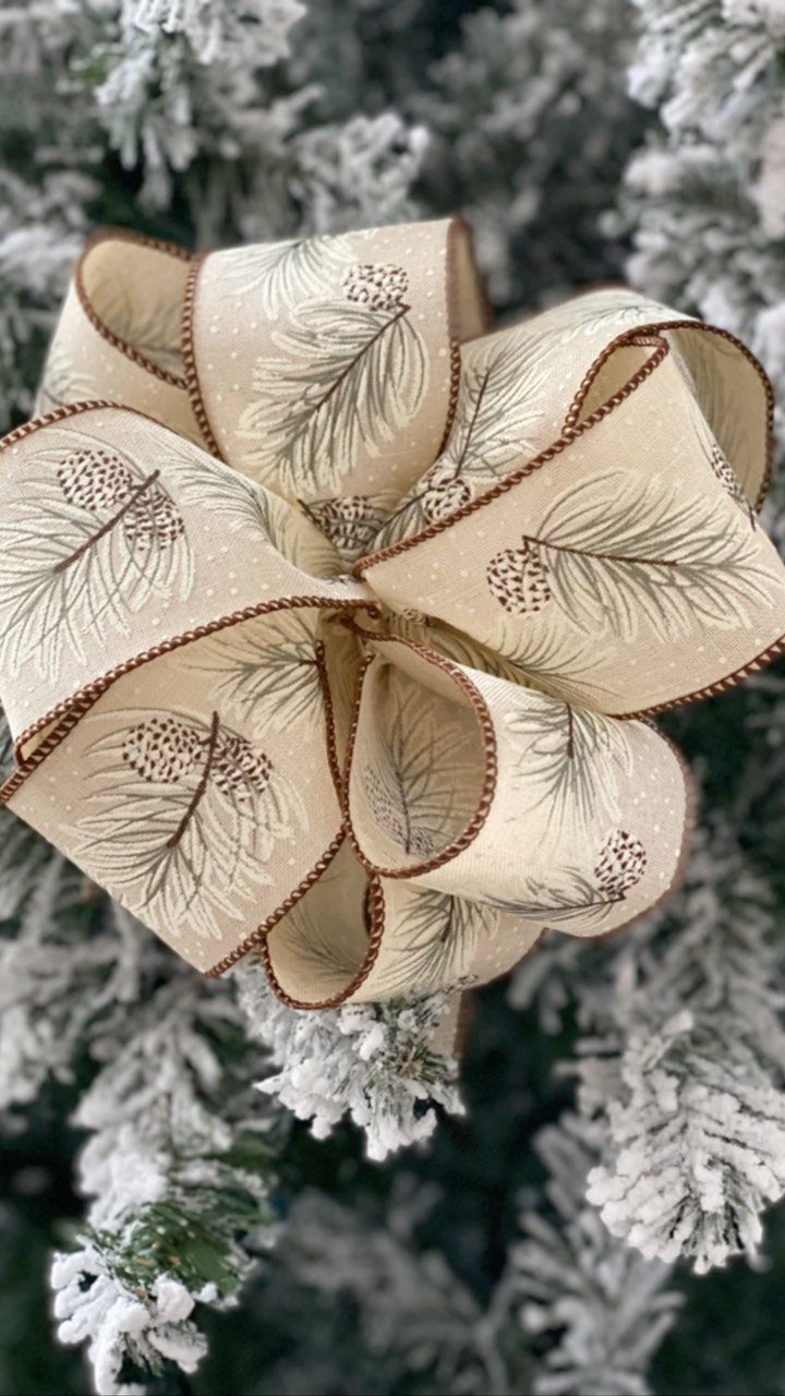 Cream fabric bow with pine patterns on a flocked Christmas tree branch